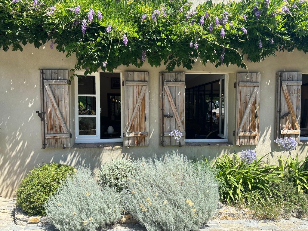 Sunlit villa facade with wooden shutters and wisteria